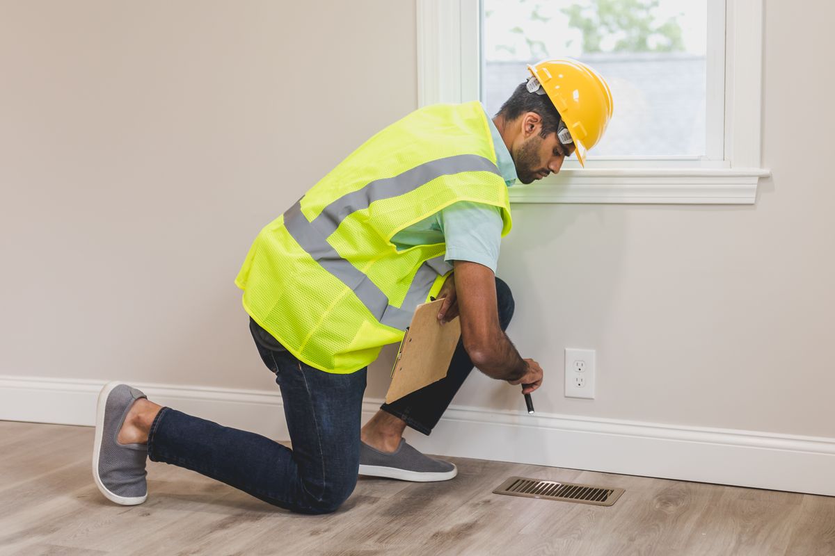 Inspector checking a wall near a floor vent
